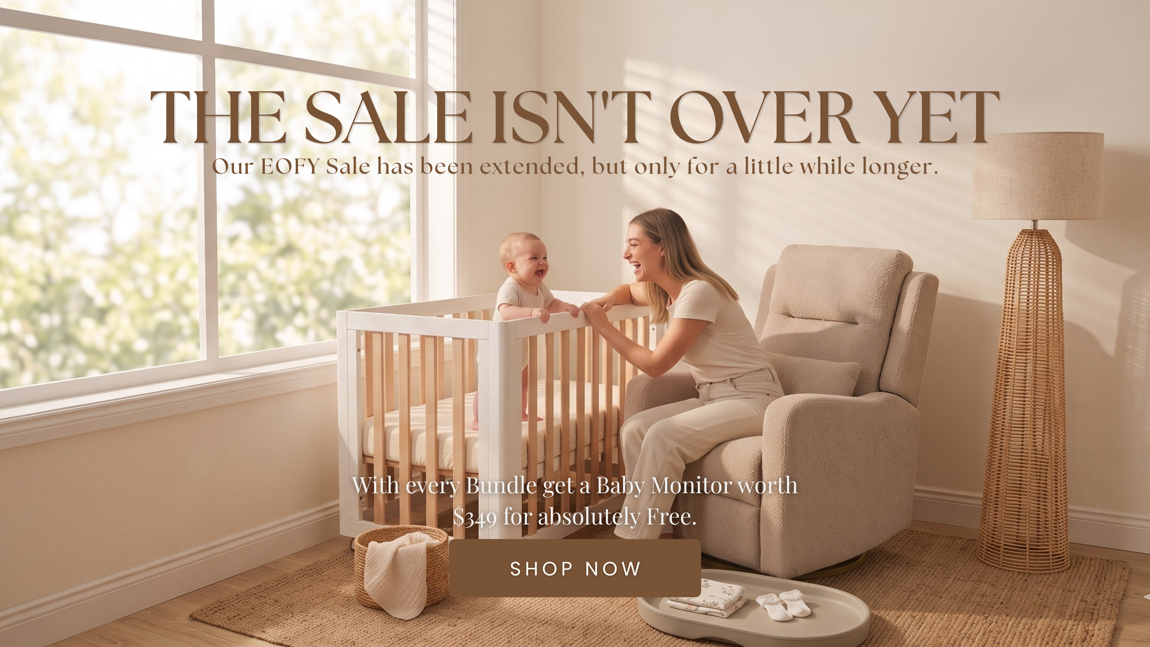 Mother smiling at a laughing baby standing in a Cocoon Piccolo cot beside a nursery recliner chair — EOFY Sale extended on Cocoon nursery furniture bundles, free baby monitor worth $349 with every bundle purchase.
